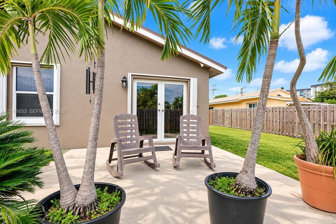 Concrete patio featuring a set of exterior French doors, an attached exterior wall-mounted light fixture, and an adjoining lawn enclosed by a wooden fence