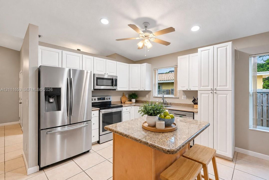 Kitchen featuring white cabinetry, stone-finish countertops, stainless steel appliances, a center island, and ceramic tile flooring