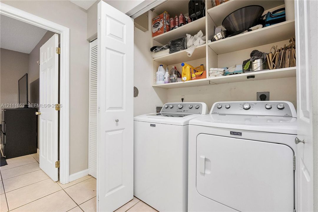 Laundry area featuring ceramic tile flooring, built-in overhead storage shelving, and bi-fold closet doors