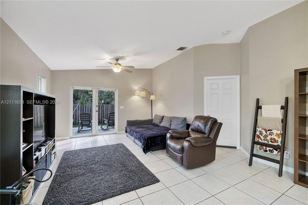 Living area featuring vaulted ceilings, neutral wall tones, large-format tile flooring, a center-mounted ceiling fan, and double-glass doors providing patio access