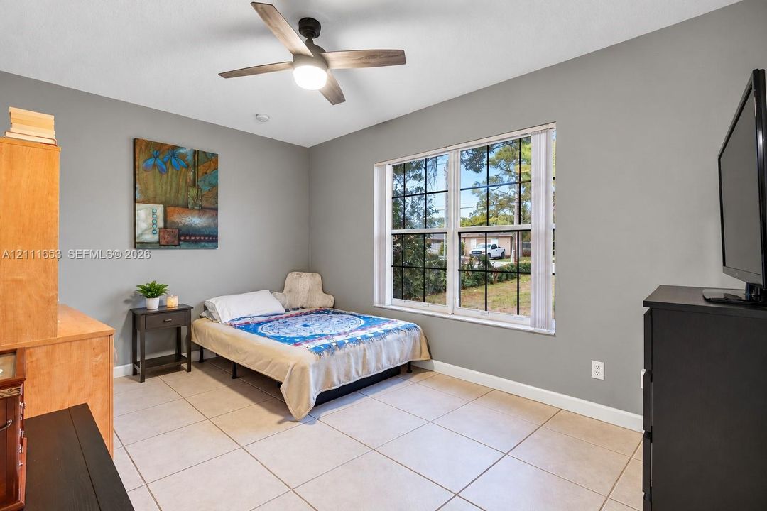 Bedroom 3 Neutral-toned walls featuring large-format ceramic tile flooring, a multi-pane window with grid detailing, and a modern ceiling fan with integrated lighting