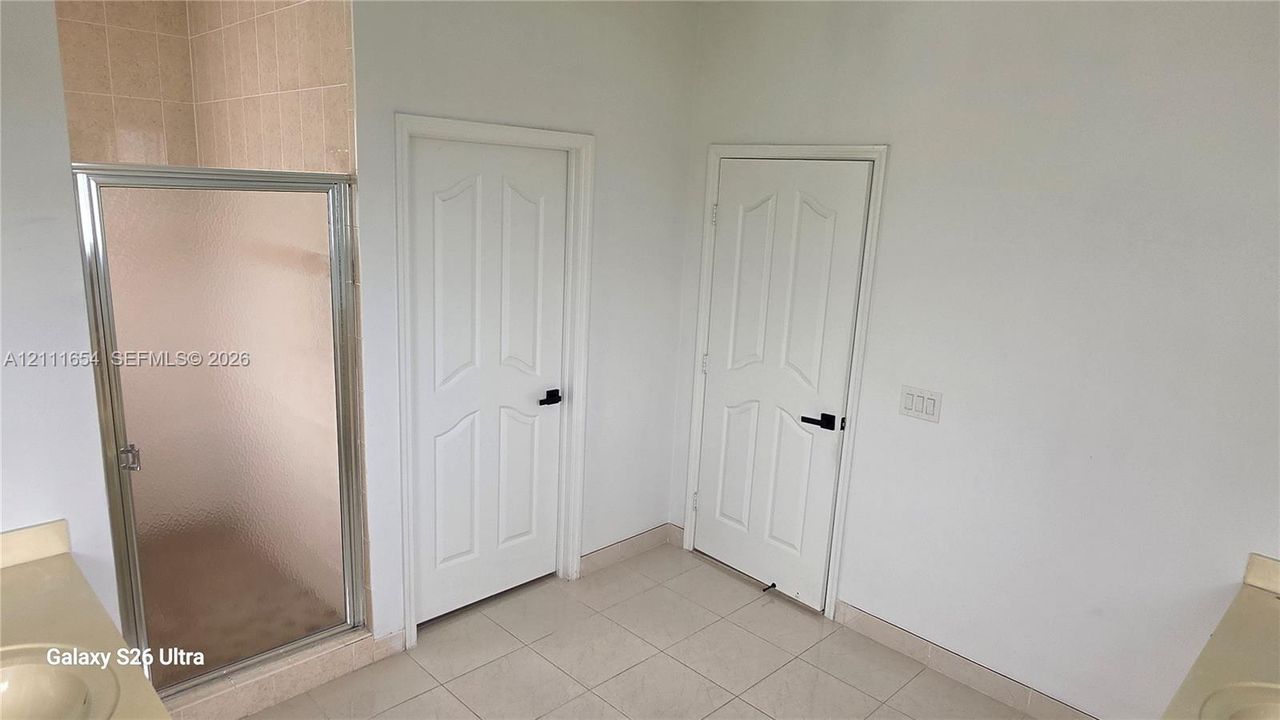 Enclosed shower stall with tiled interior and metal-framed glass door, light-toned ceramic tile flooring, and two white paneled interior doors featuring matte black hardware