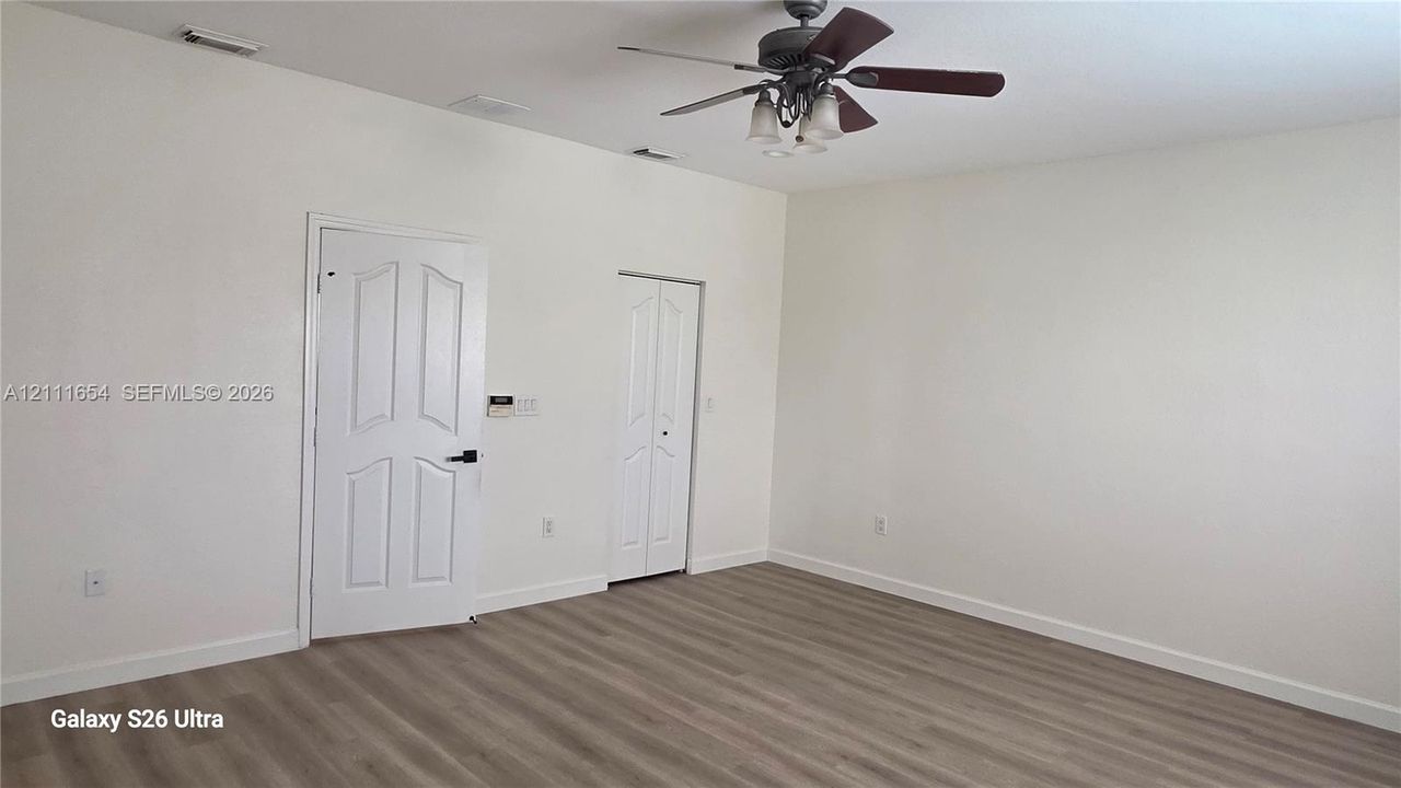 Neutral-toned wood-finish flooring, ceiling fan with integrated lighting, multi-panel door, and bi-fold closet door