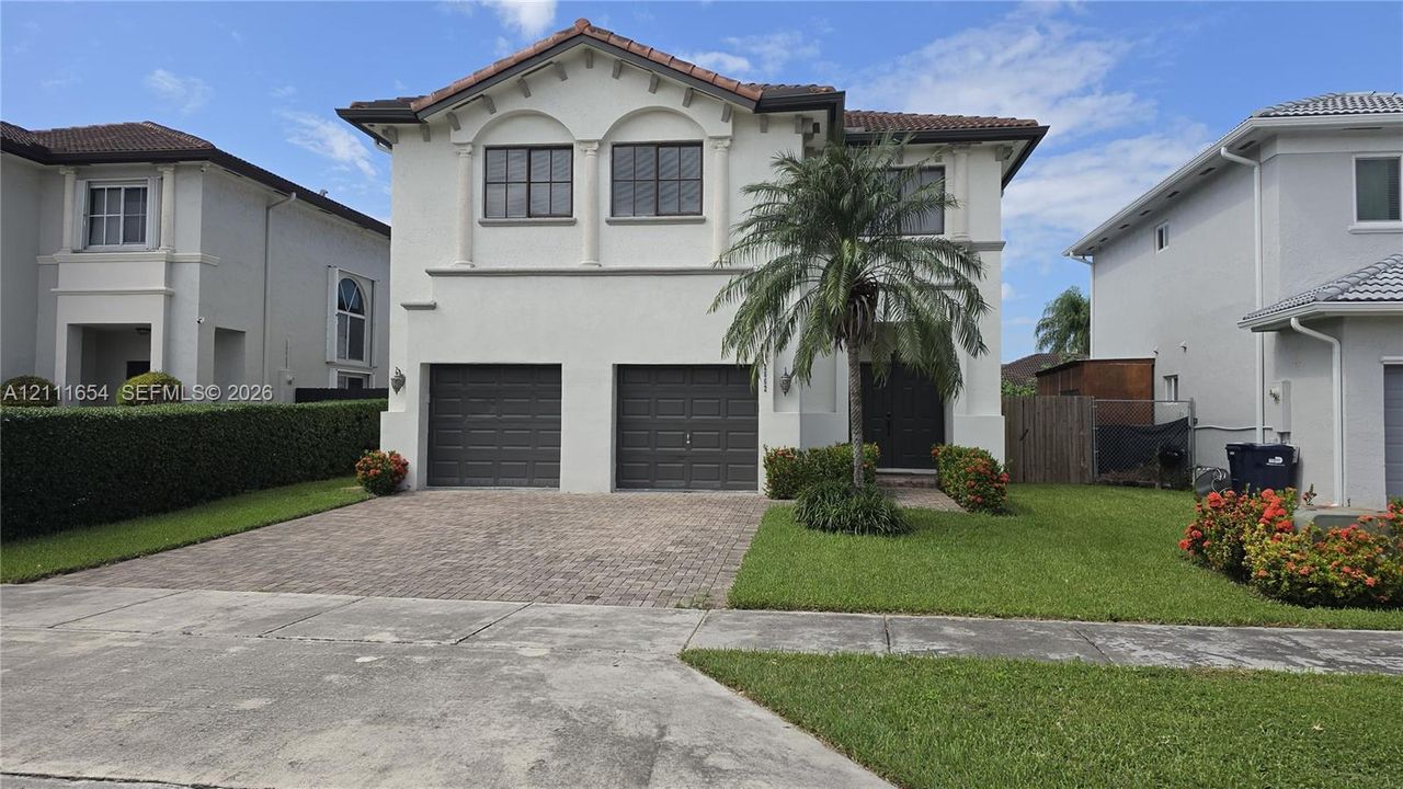Two-story stucco exterior featuring arched upper-level windows, a tile roof, a paved driveway, and a two-car garage