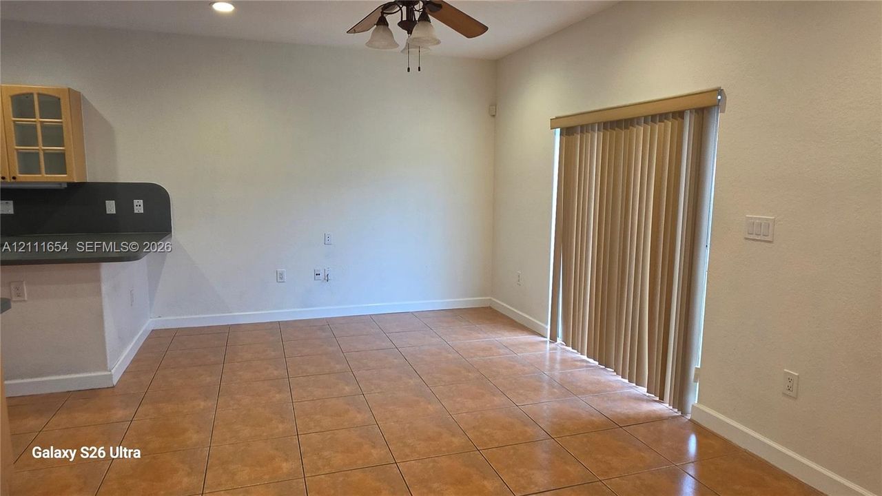 Tiled flooring, sliding glass patio door with vertical blinds, ceiling fan with light fixture, and kitchen counter with upper cabinet cabinetry