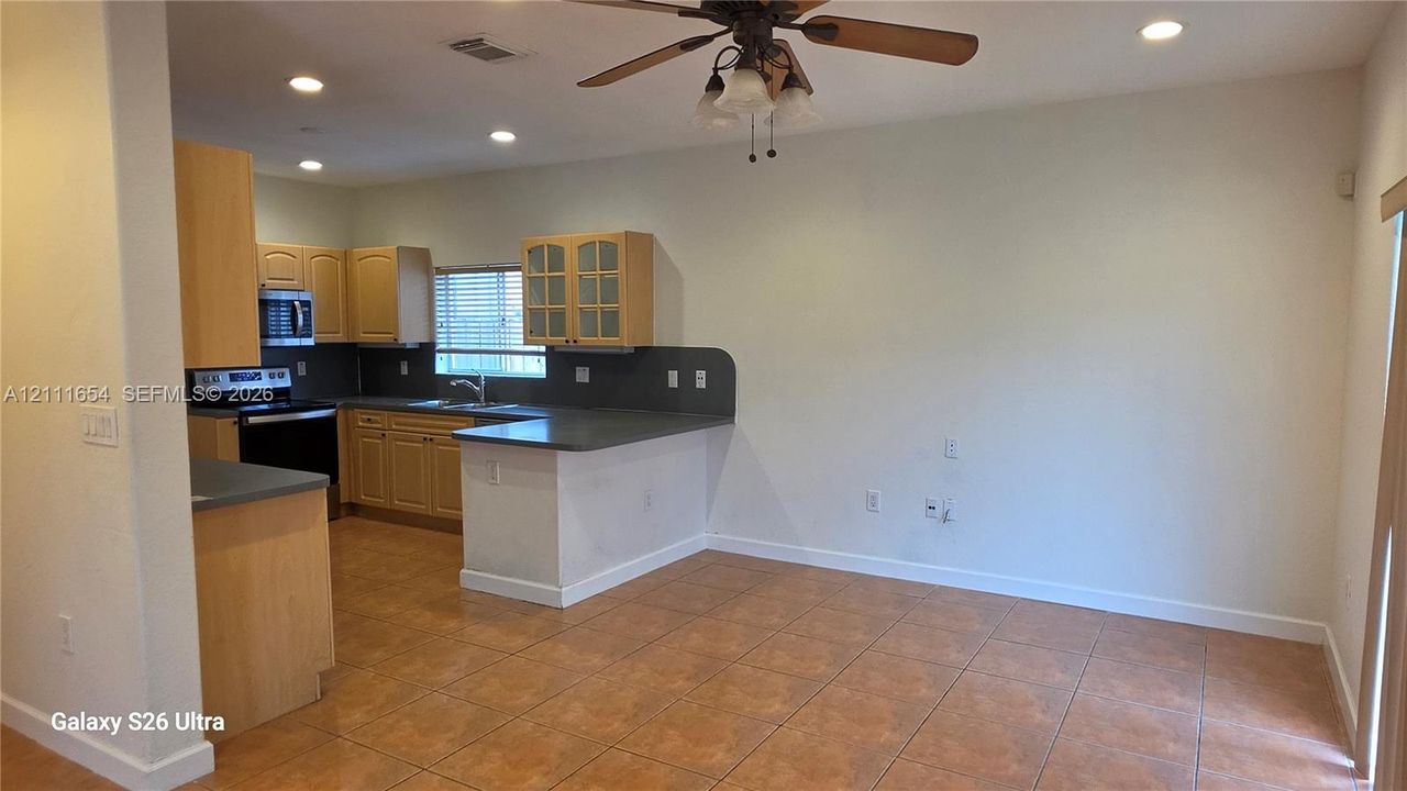 Kitchen area featuring wood cabinetry, glass-panel upper cabinet doors, solid-surface countertops, tile flooring, and a ceiling fan with integrated light fixture