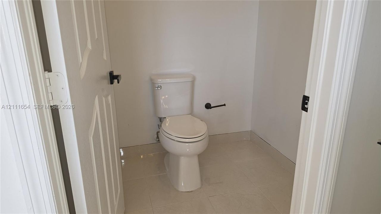 Restroom featuring a two-piece white toilet, tile flooring, and matte black door hardware and accessories