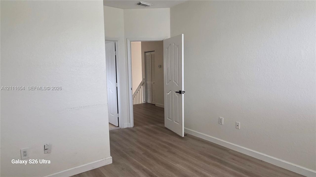 Neutral-toned interior space featuring wood-finish flooring, white walls, and six-panel interior doors with black hardware