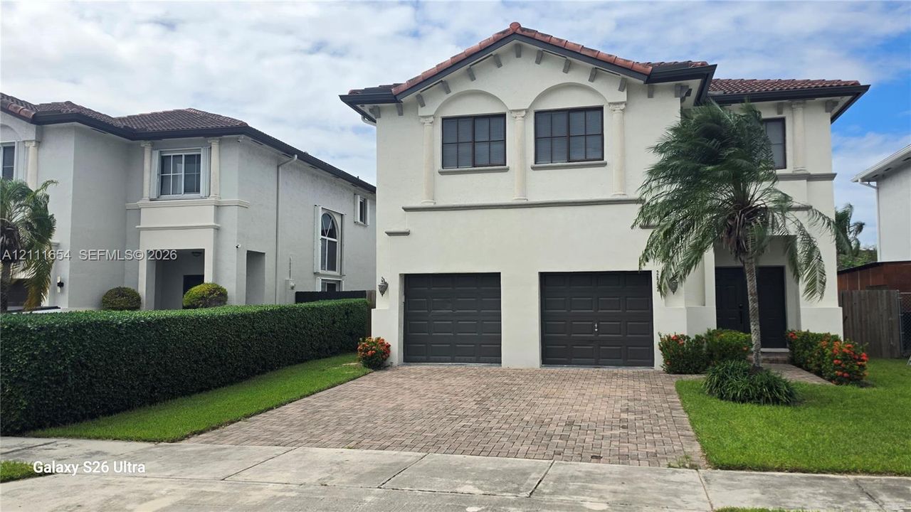 Two-story stucco exterior featuring a tile roof, dual-car garage with paneled doors, and a decorative arched window detail