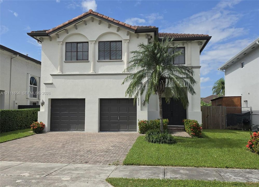 Two-story stucco exterior featuring a tiled roof, arched window detailing, two-car garage, and paver driveway