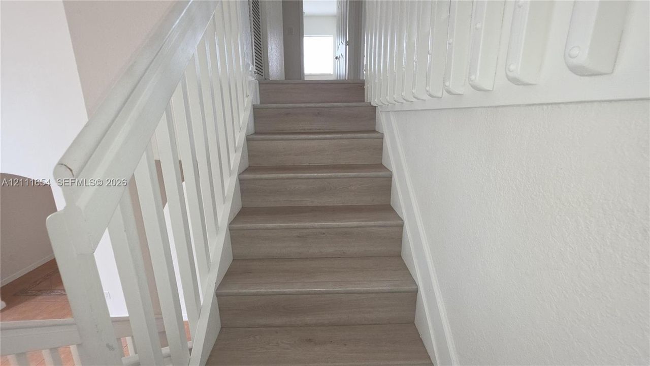 Staircase featuring wood-finish treads and white balustrades with a matching handrail