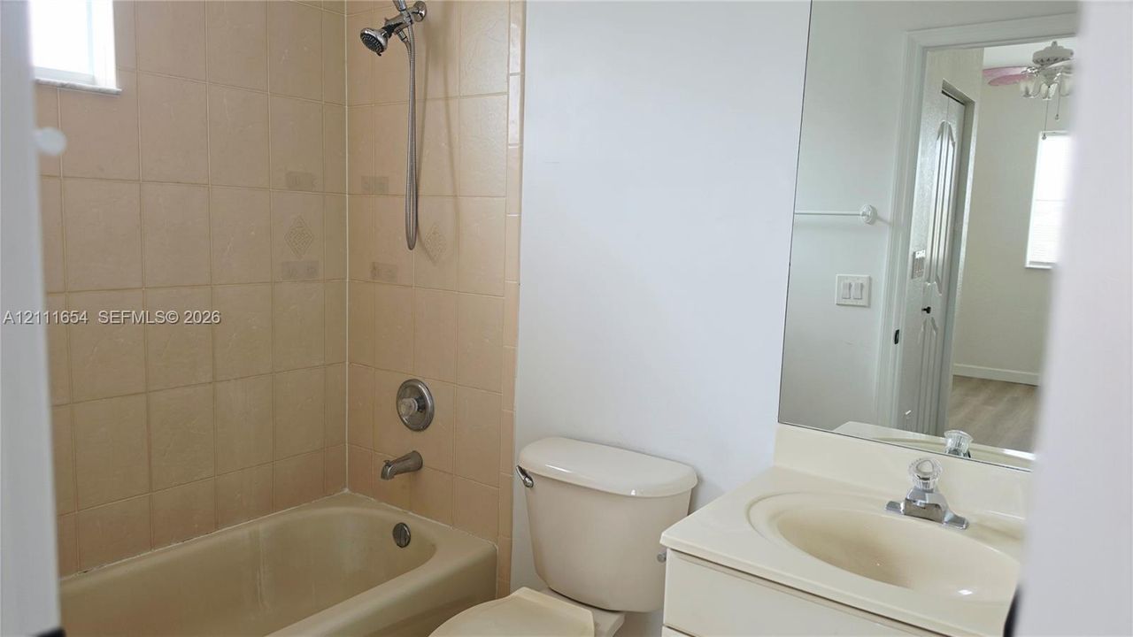 Bathroom featuring a tub-shower combination with tile surround, vanity with an integrated basin, and a large wall-mounted mirror
