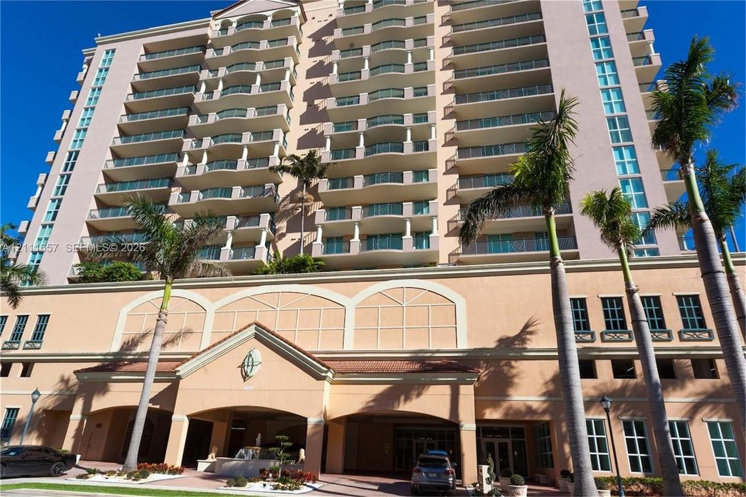 High-rise condominium exterior featuring stucco facade, recessed private balconies with glass railings, arched architectural detailing, and a covered porte-cochère entry