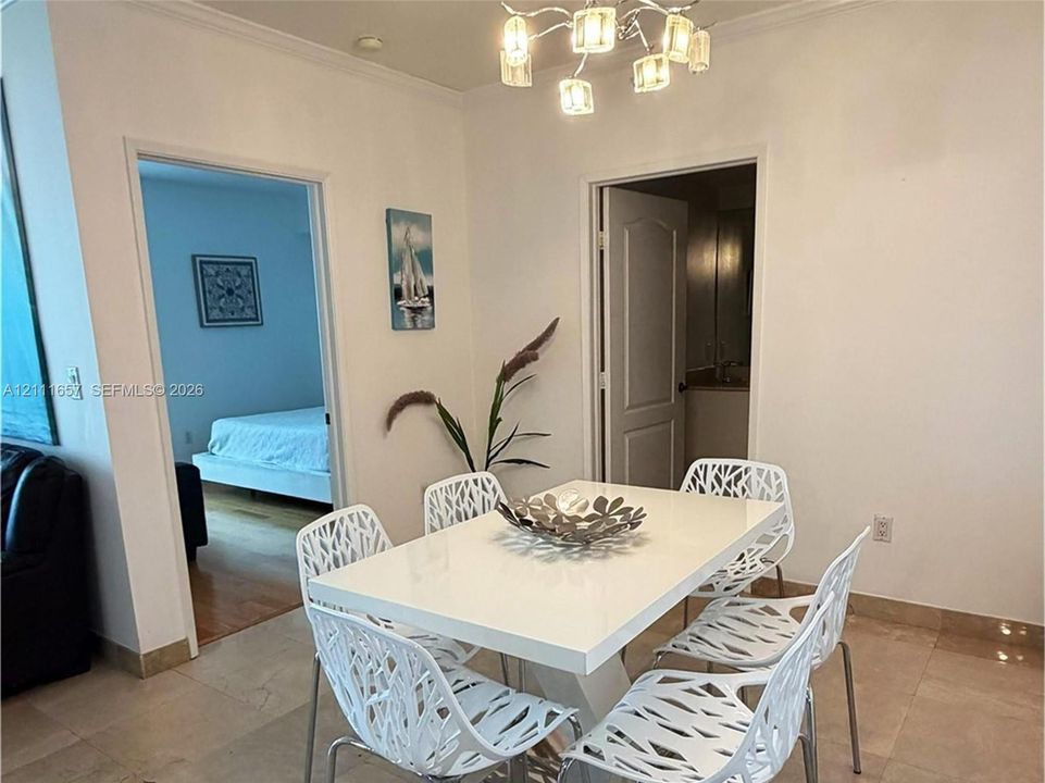 Dining area featuring large-format light-toned stone tile flooring, crown molding, and a contemporary six-light multi-arm chandelier