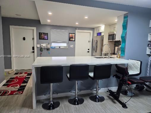Kitchen featuring a white waterfall-edge peninsula, integrated stainless steel appliances, recessed ceiling lighting, and ceramic-finish flooring