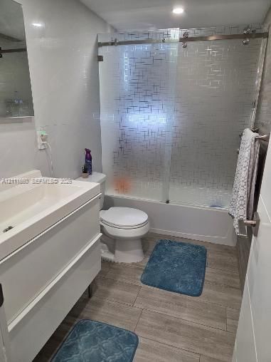Modern white wall-mounted vanity with a rectangular sink, sliding glass shower door with etched geometric detailing, wood-finish flooring, and recessed ceiling lighting