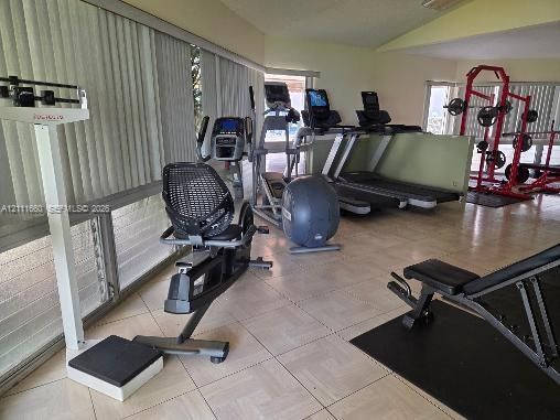 Fitness room featuring light-toned ceramic tile flooring and floor-to-ceiling windows with vertical blinds