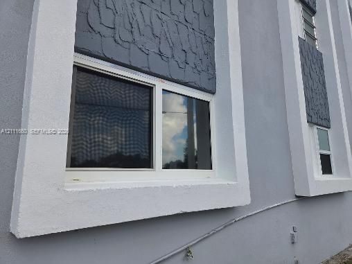 Exterior featuring smooth stucco wall finish, contrasting textured masonry panels, and windows framed in thick, white architectural molding