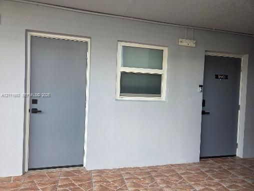 Exterior entry featuring two solid-core doors with matte black hardware, dual-pane window with white framing, and stone-tile flooring