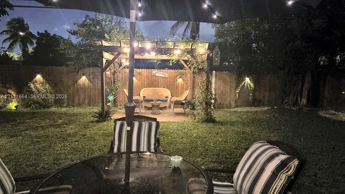 Private backyard featuring a wooden pergola, perimeter wood fencing, and mounted wall lighting