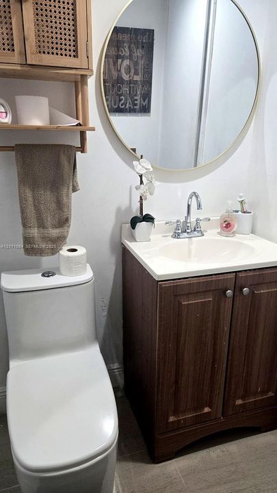 Vanity featuring wood-finish cabinetry, light-toned countertop with an integrated basin, circular mirror with a metallic frame, and wall-mounted cane-accented shelving