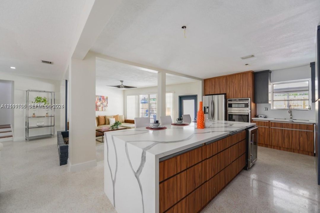 Kitchen featuring a central island with a stone-finish countertop and waterfall edge, wood-finish cabinetry, stainless steel built-in wall oven, and light-colored terrazzo flooring