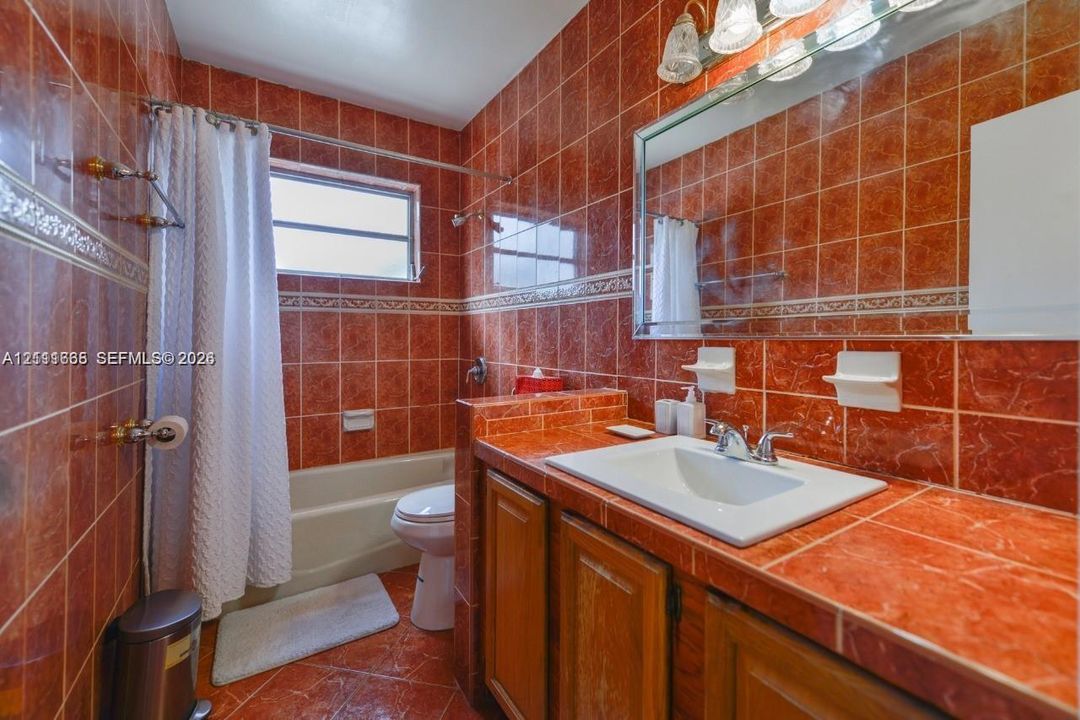 Bathroom featuring full-height decorative tile wall finishes, an integrated vanity countertop with a drop-in sink, wood-finish cabinetry, a large wall-mounted mirror, and a soaking tub with shower combination