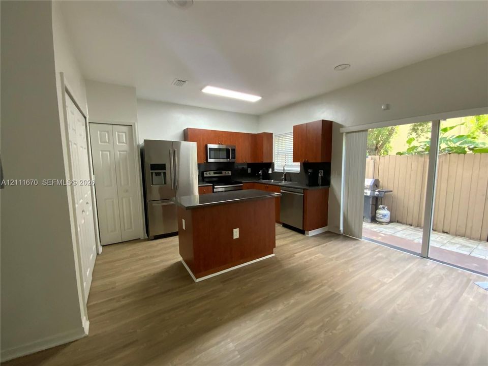 Kitchen featuring wood-finish cabinetry, central island with stone countertop, stainless steel appliances, and sliding glass door access to a fenced patio