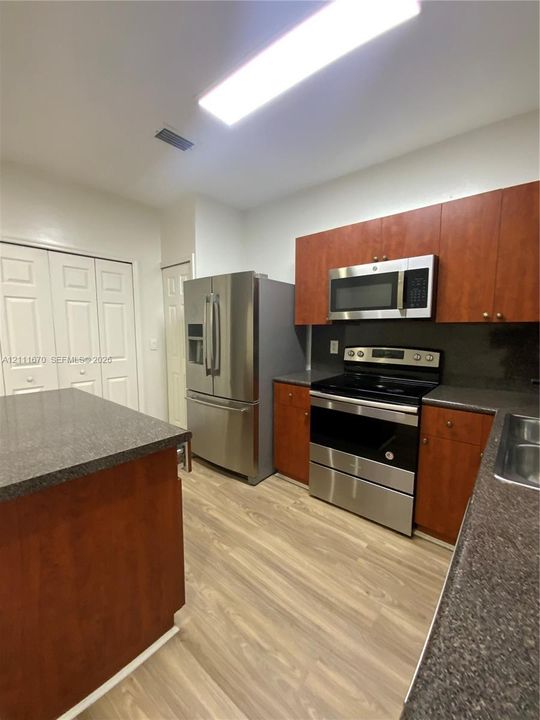 Kitchen featuring wood-finish cabinetry, stainless steel appliances, dark stone-finish countertops, wood-finish flooring, and a central island