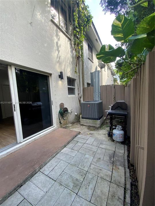 Paved patio with light-toned stone-finish pavers, sliding glass door entry, exterior wall-mounted lighting, and privacy fencing