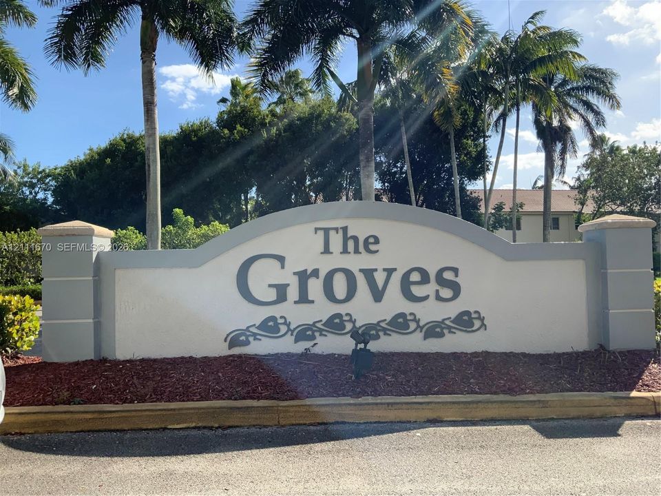 Stucco community entrance monument featuring decorative lettering, tiered concrete pillars, and established palm trees