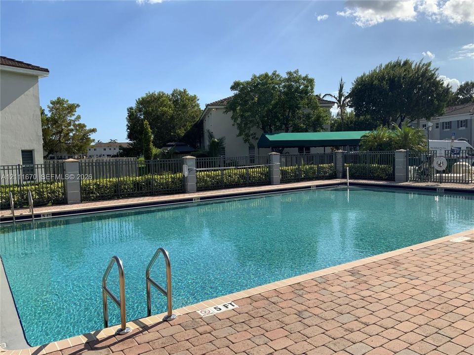 Swimming pool featuring metal ladders, paver decking, and perimeter metal fencing