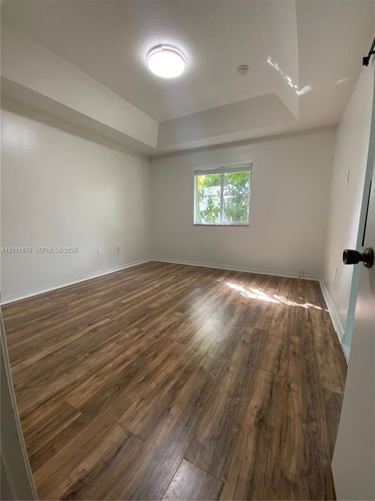 Room featuring a recessed tray ceiling, wood-finish flooring, and a single window with integrated blinds