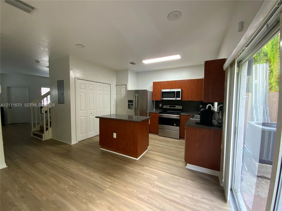 Kitchen featuring wood-finish cabinetry, a center island with a stone-top surface, stainless steel appliances, and wood-finish flooring