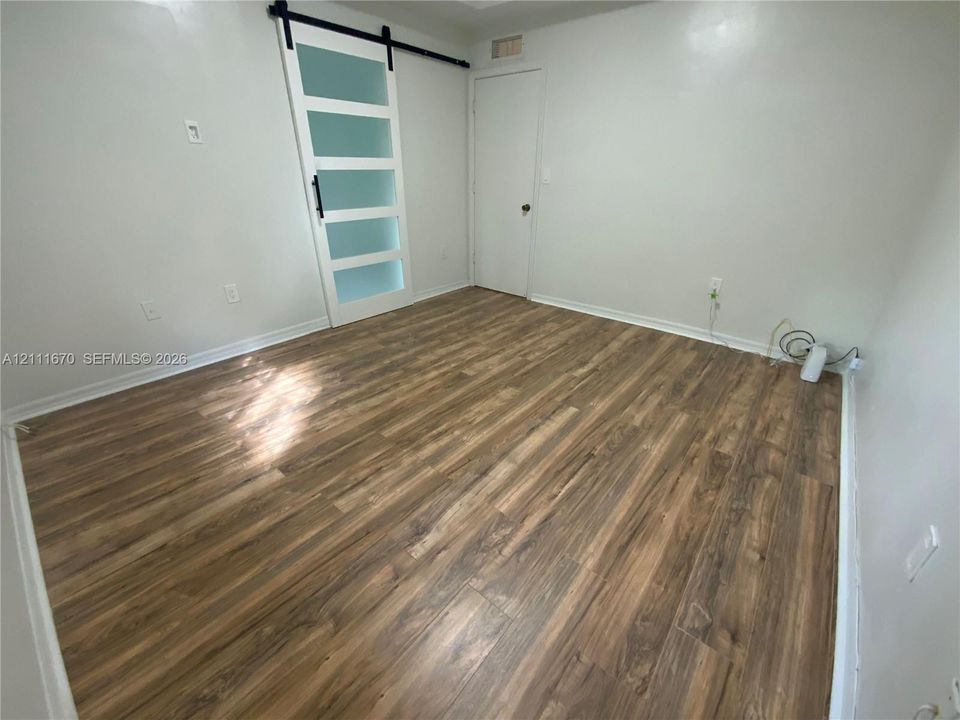 Master  Bedroom wood-finish flooring, a sliding barn door with glass panes, and a traditional door with a matte black handle