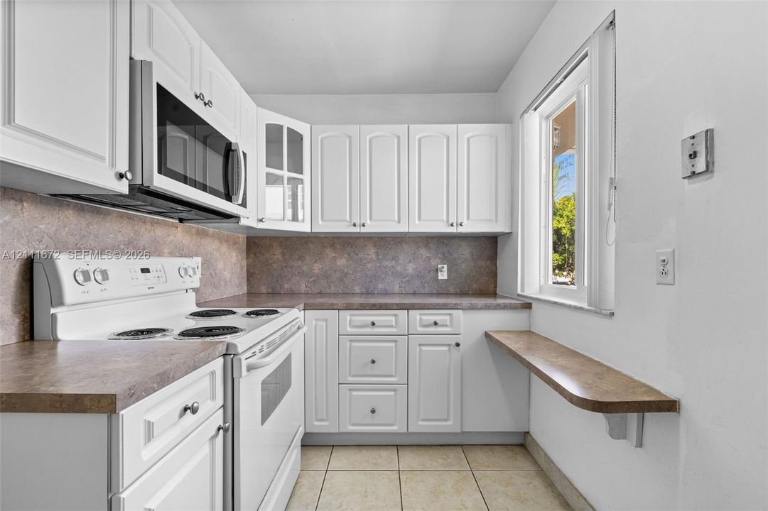 Kitchen featuring white cabinetry, solid-surface countertops, tile flooring, a built-in microwave, and a wall-mounted breakfast bar