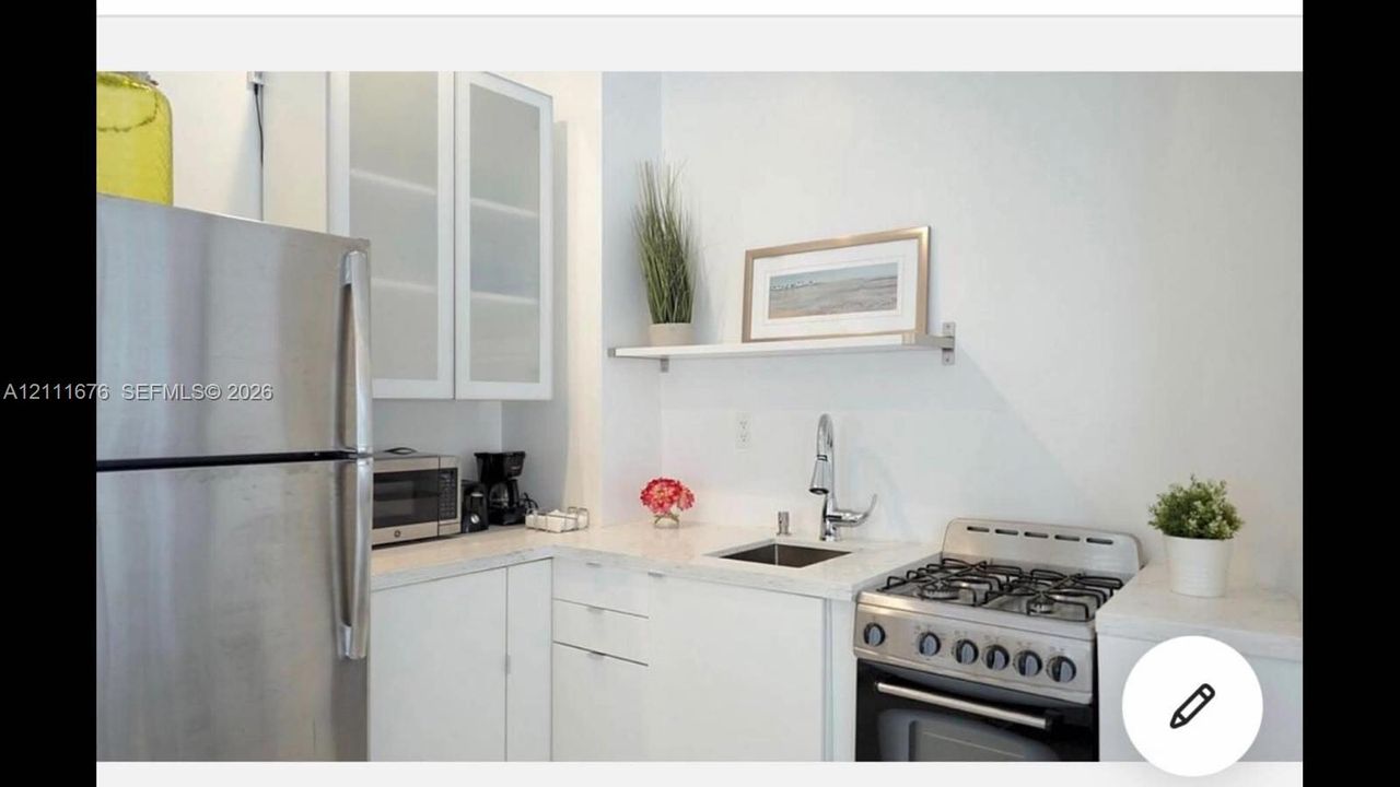 Kitchenette featuring white flat-panel cabinetry, stainless steel appliances, light-toned countertops, undermount sink with high-arc faucet, and built-in wall shelving