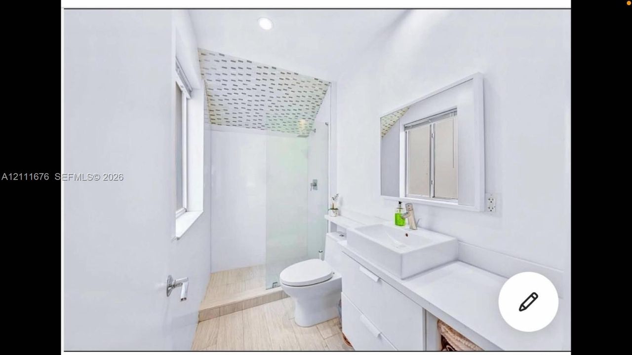 Bathroom featuring a wall-mounted vanity with a rectangular vessel sink, glass-enclosed shower, patterned ceiling tile, and wood-finish flooring