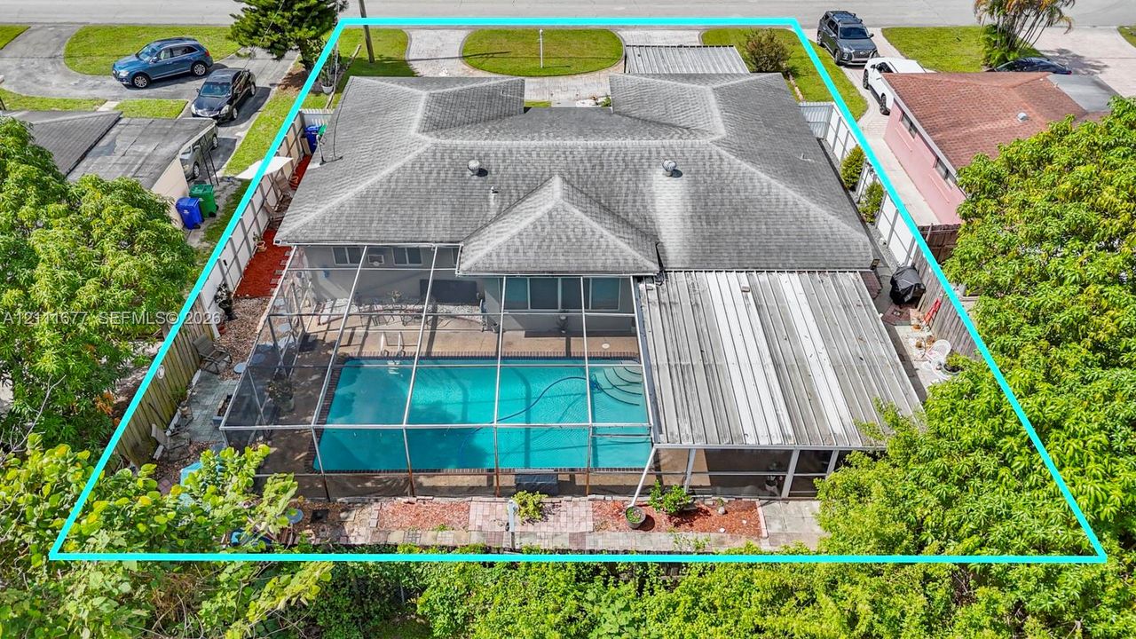 Aerial view of property featuring a screened-in swimming pool, covered patio, fenced perimeter, and shingled roof