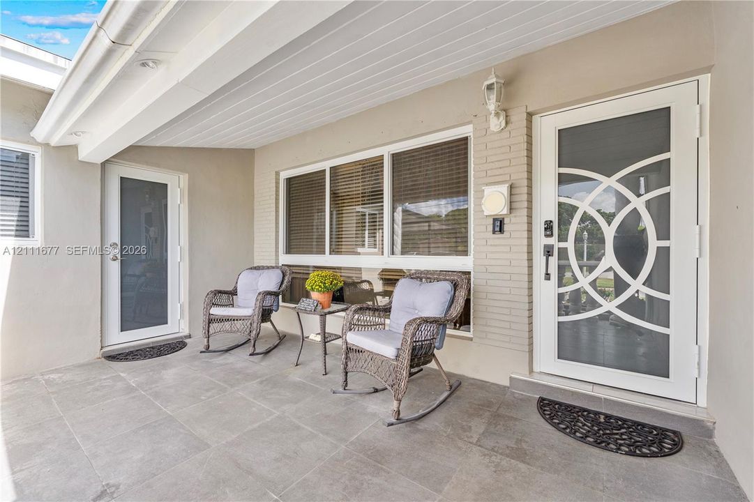 Covered porch featuring large-format tile flooring, white brick accents, and two exterior doors with decorative circular-patterned glass inserts