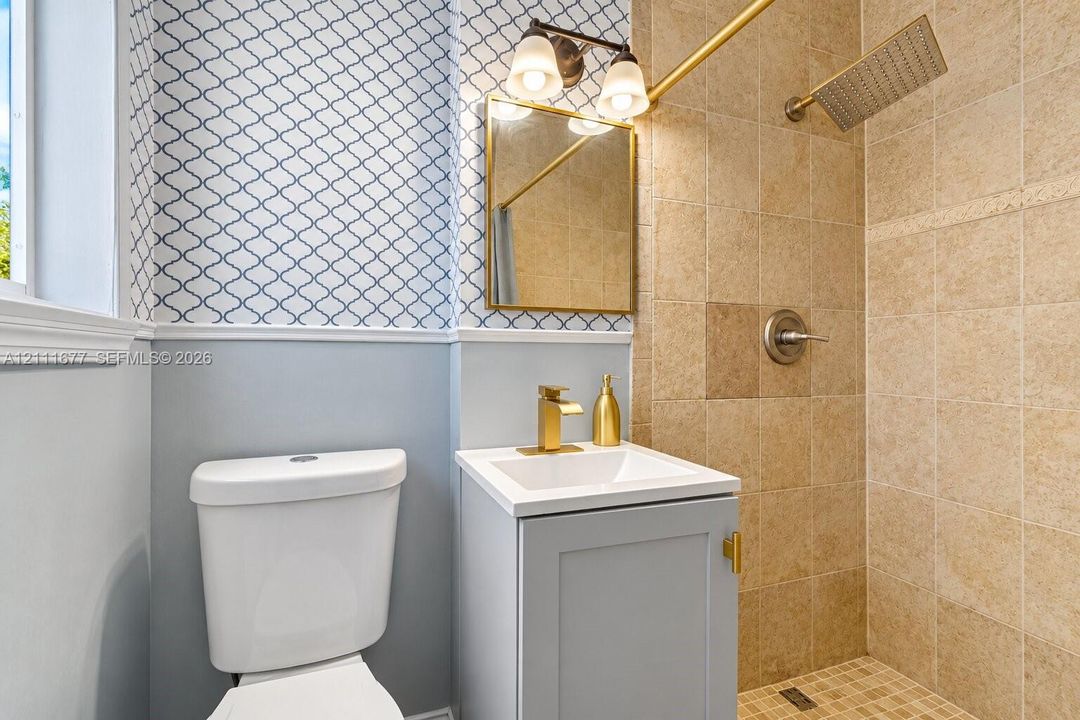 Bathroom featuring a vanity with a white rectangular basin, brass-finish faucet, framed wall-mounted mirror, two-light fixture, and a walk-in shower with square tile surround and rainfall showerhead