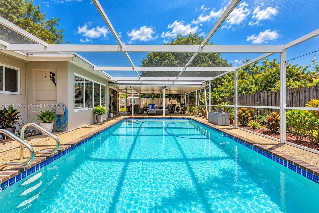 Screened lanai featuring a swimming pool, tiled pool coping, metallic handrails, and a covered patio area