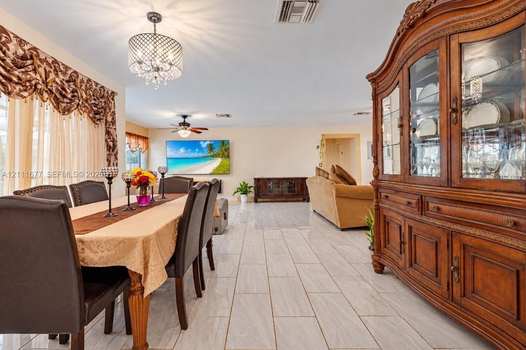 Open-concept room featuring light-toned tile flooring, a multi-tier crystal chandelier, and a ceiling fan with integrated lighting