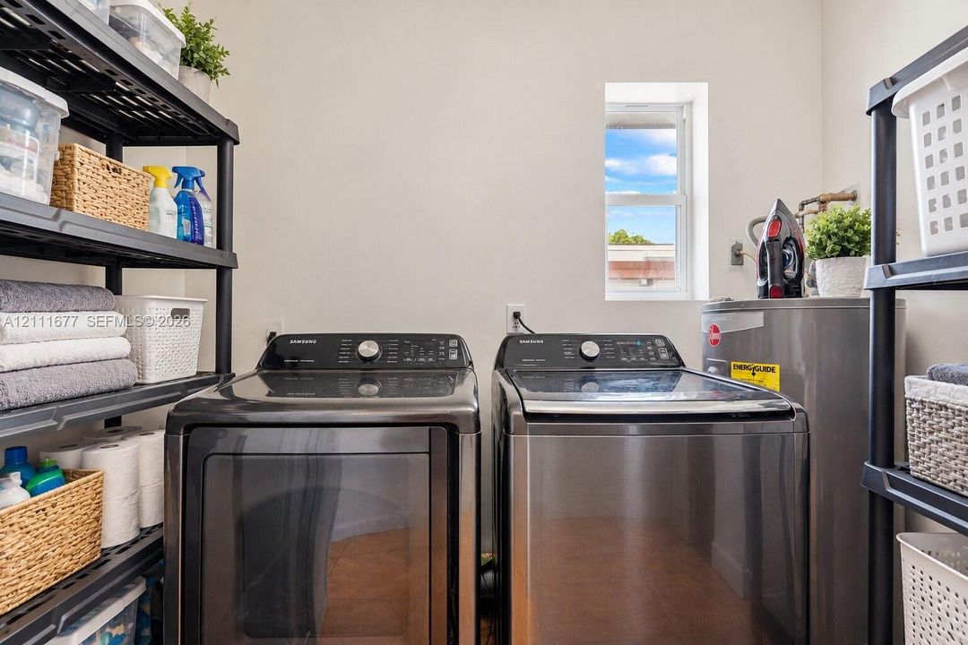 Laundry area featuring stainless steel washer and dryer, tile flooring, and natural light from a vertical window