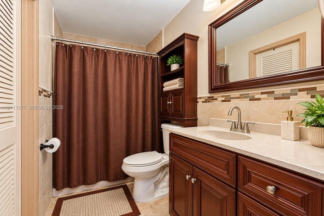 Bathroom featuring a vanity with wood-finish cabinetry, light-toned countertop, integrated shelving, framed wall mirror, and decorative tile backsplash
