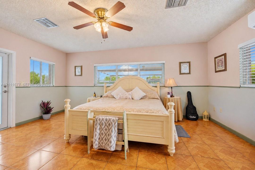Spacious room featuring large-format ceramic tile flooring, neutral wall paneling with a chair rail, multi-pane windows, and a ceiling fan with integrated lighting