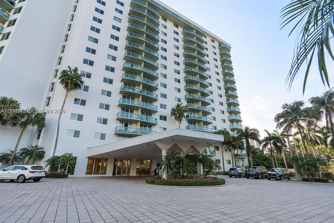 High-rise exterior featuring a tiered façade with private glass-railed balconies, a covered porte-cochère entry, and a paved arrival plaza with circular landscaping