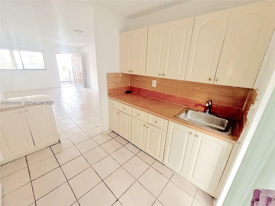 Kitchen featuring light-toned cabinetry, wood-surface countertops, an integrated stainless steel sink, and ceramic tile flooring