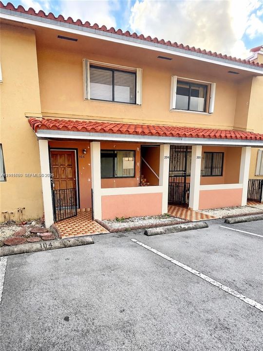 Two-story building exterior featuring a tiled roof, stucco facade, covered front entryways, and metal security door grilles