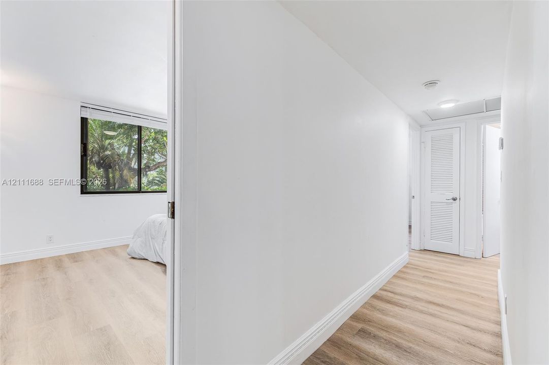 Interior space featuring wood-finish flooring, a white louvered door, recessed lighting, and a window with exterior greenery